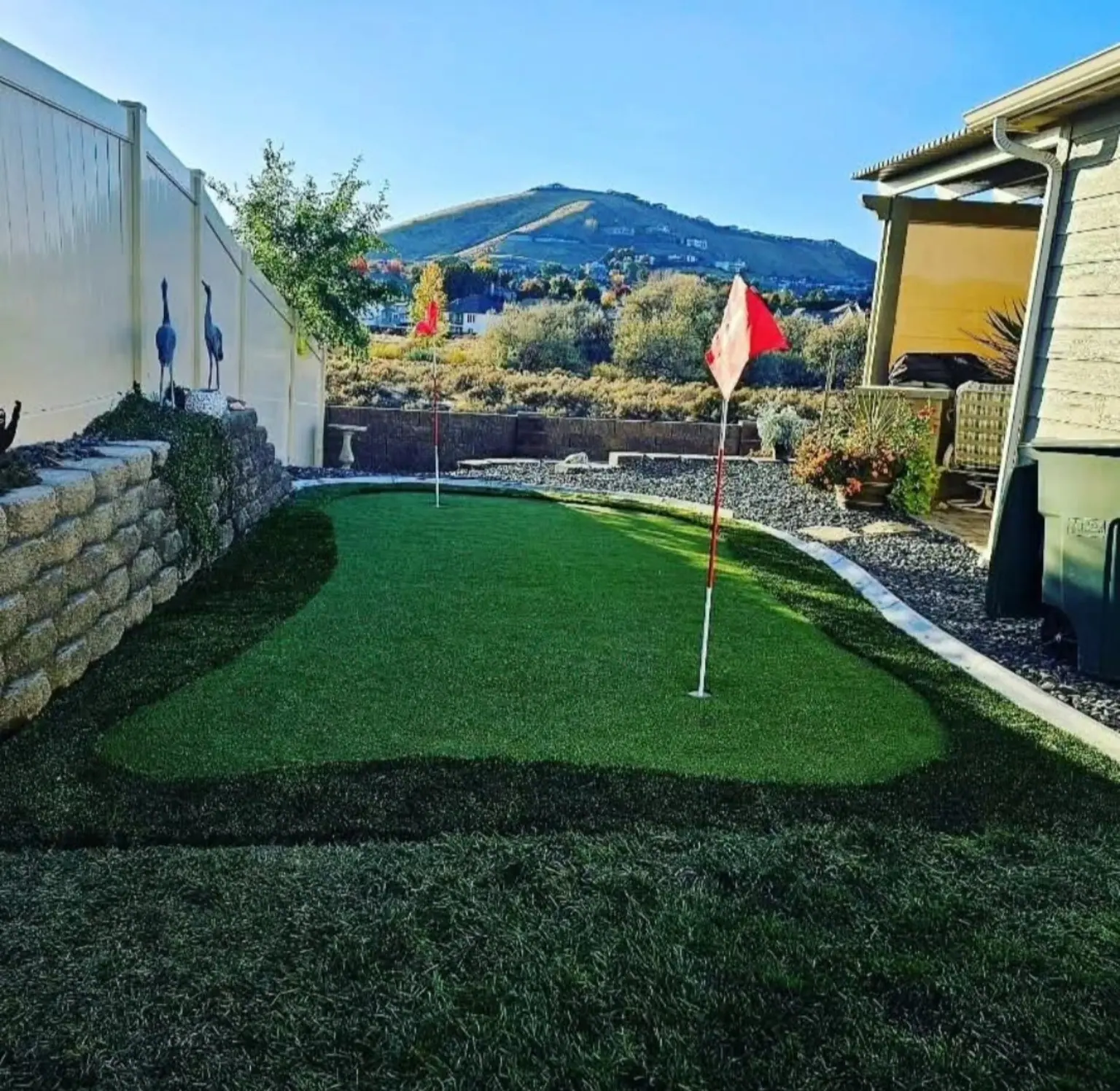 Backyard putting green with a flag beside a block wall
