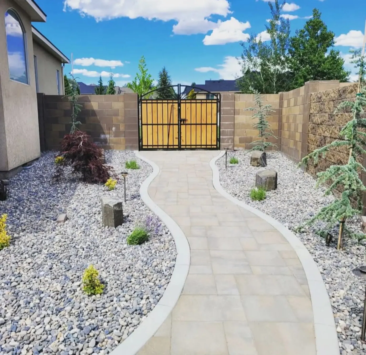 Curving paver walkway through gravel beds to a gate